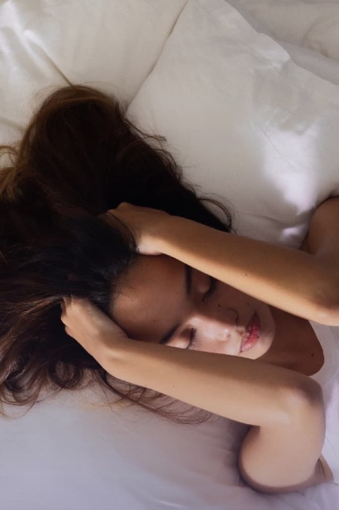 Frau liegt im Bett und hält sich mit beiden Händen den Kopf